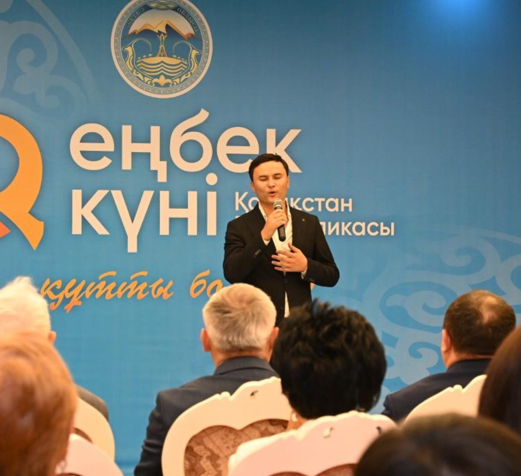 «Еңбек күні» шарасында микрофонмен сөйлеп тұрған адам және тыңдаушылар.