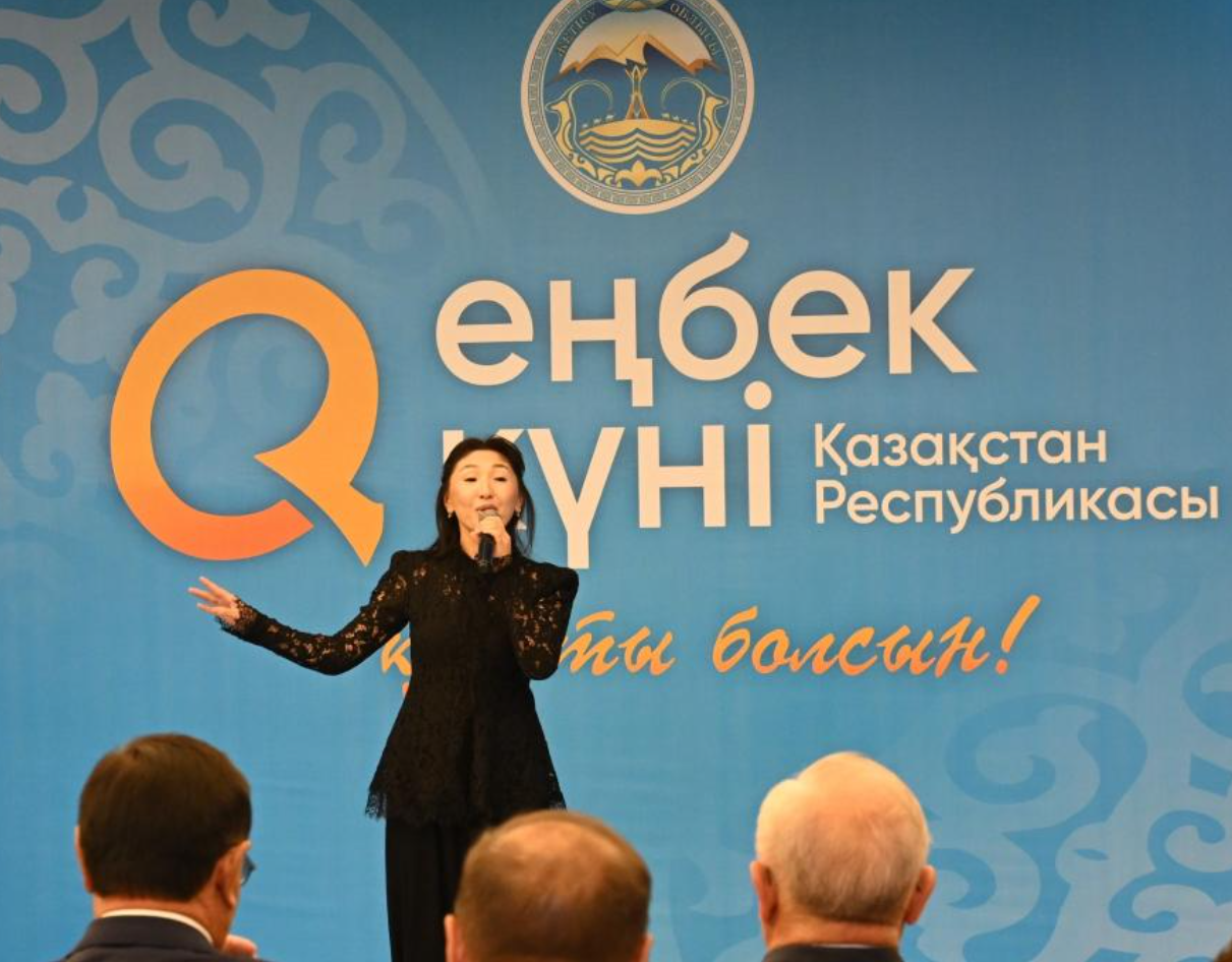 «Еңбек күні» мерекелік іс-шарасында сахнада сөйлеп тұрған әйел.