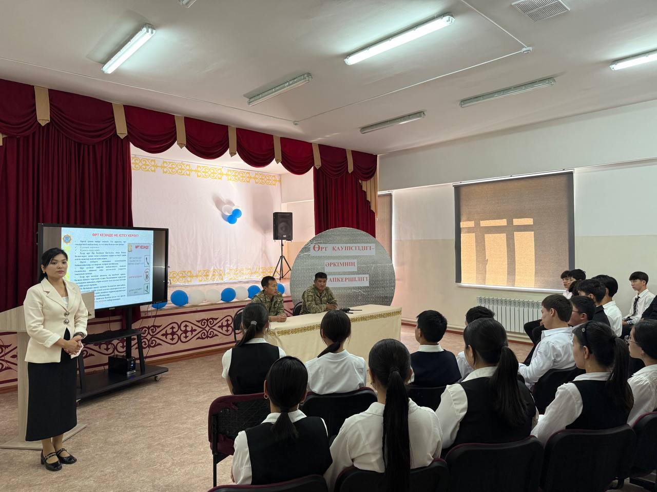 Мектеп акт залында оқушыларға өрт қауіпсіздігі бойынша өткізіліп жатқан презентация.
