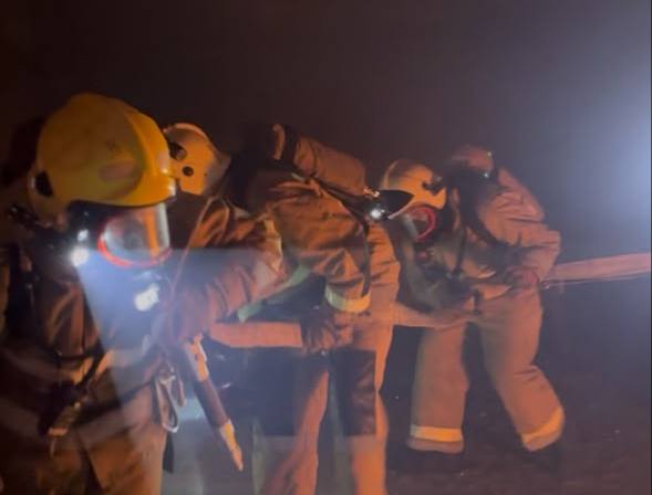Арнайы киімі мен шлем киген өрт сөндірушілердің тобы түтін арасында жұмыс істеп жатыр.