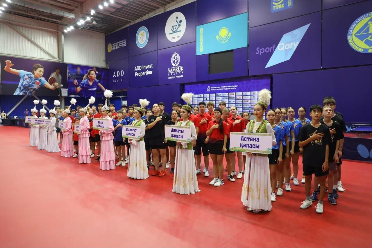 Спорттық аренада ұлттық киімдегі қыздар мен спортшылардың қатар тұрған сәті.