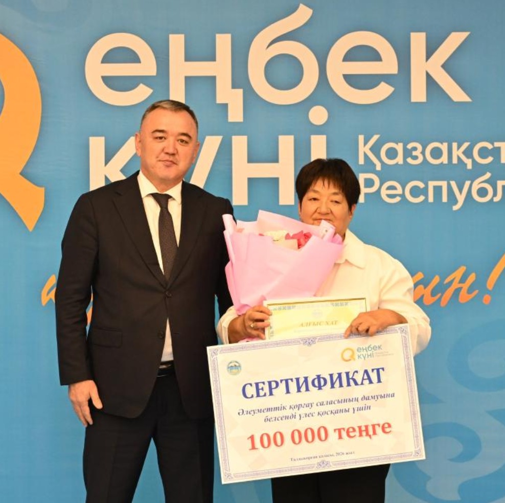 «Еңбек күні» мерекесінде әйел адамға 100 000 теңгелік сертификат пен гүл шоғы табысталып жатқан сәт.