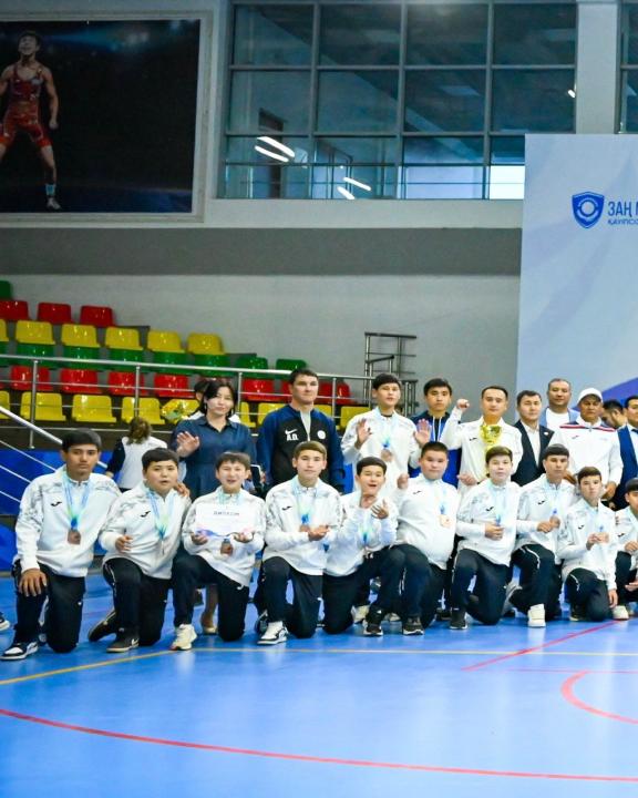 Спорт залында медаль алған жас күресшілер мен жаттықтырушылардың топтық суреті.