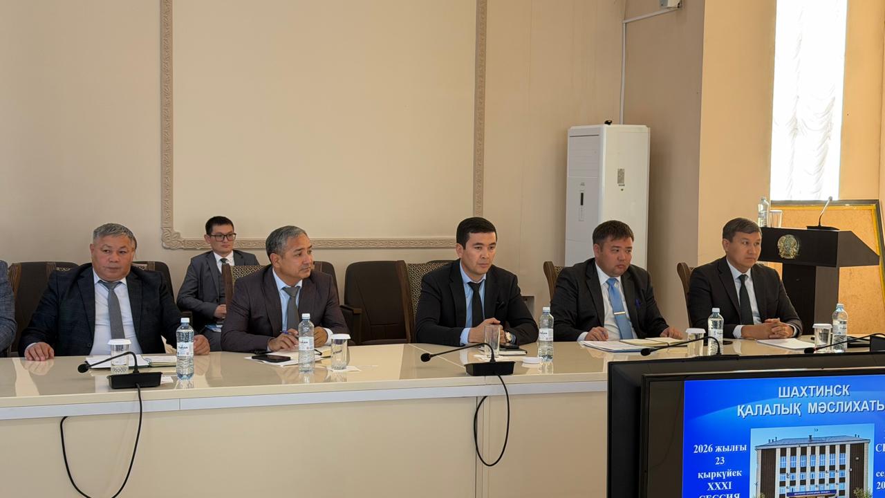 Іскерлік костюм киген адамдар тобы ресми кеңес кезінде презентация көрсетіліп жатқан экранның алдында үстел басында отыр.