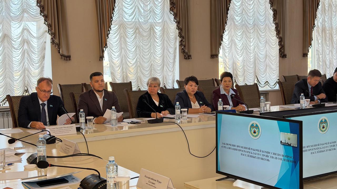 Іскерлік костюм киген адамдар тобы ресми кеңес кезінде презентация көрсетіліп жатқан экранның алдында үстел басында отыр.