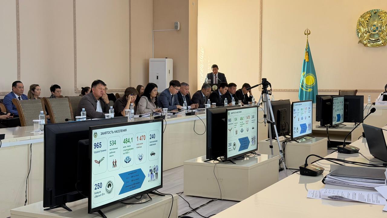 Ресми залдағы кеңестегі адамдар, олардың алдында халықтың жұмыспен қамтылуы бойынша инфографикасы бар мониторлар.