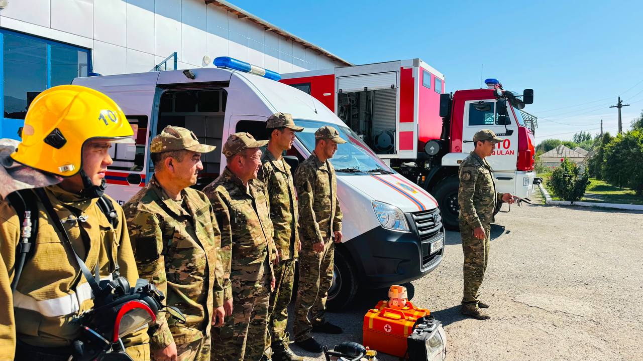 Жедел жәрдем және өрт сөндіру көліктерінің жанында тұрған әскери және құтқару қызметі қызметкерлері.