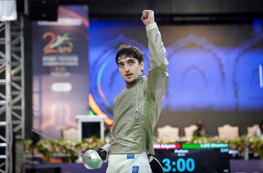 Жеңіске жеткеніне қуанған алтын түсті киімдегі семсерлеуші спортшы.