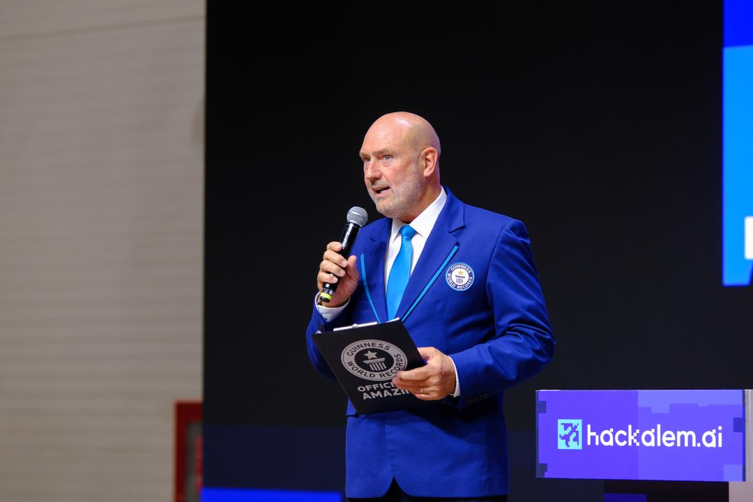 Көк костюм киген Гиннес әлемдік рекордтарының ресми өкілі микрофонмен сөйлеп тұр.