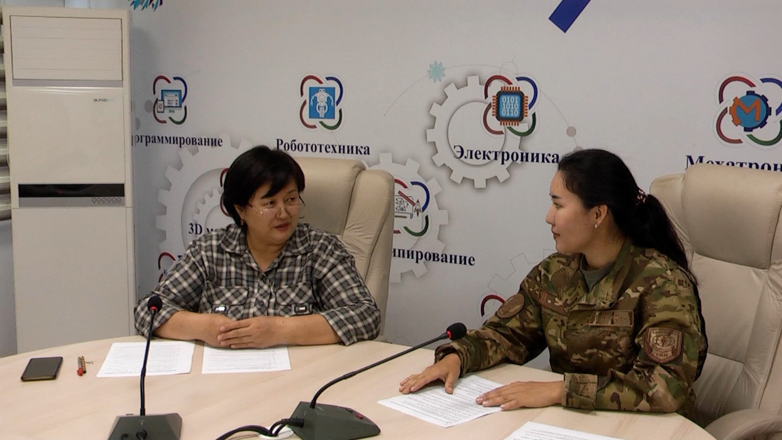 Келіссөз жүргізіп жатқан әкімшілік қызметкер мен әскери формадағы әйел.