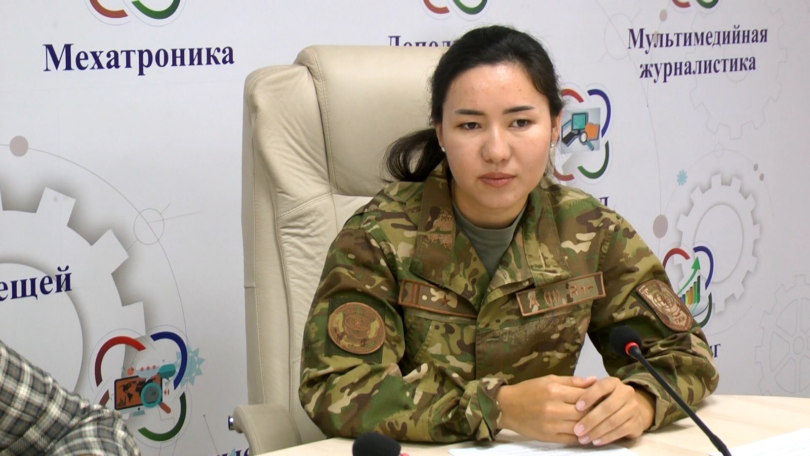 Камуфляж киген әйел офицер баспасөз мәслихатында отыр.