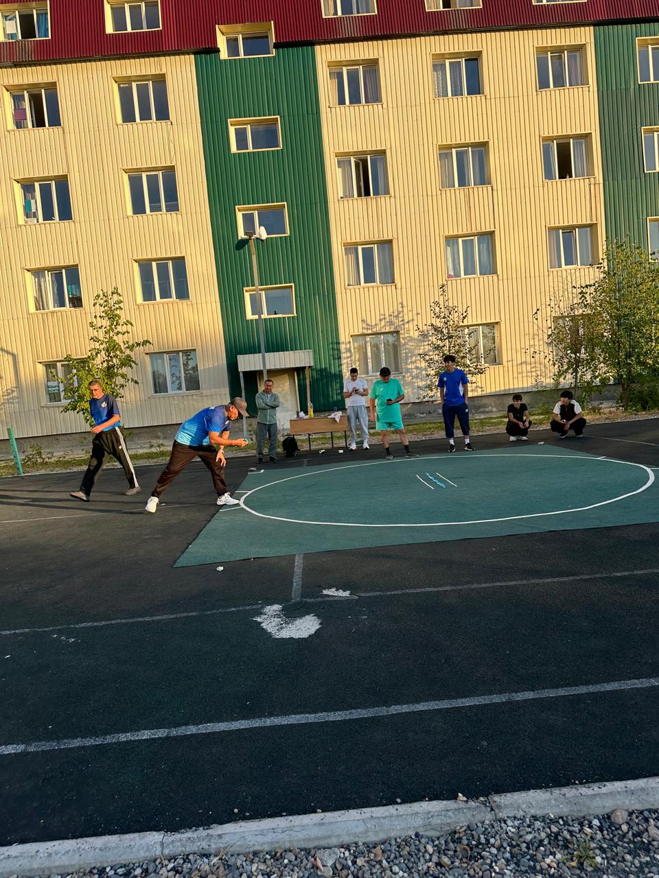Үйдің алдындағы спорт алаңында боккинг ойынын ойнап жатқан жастар.