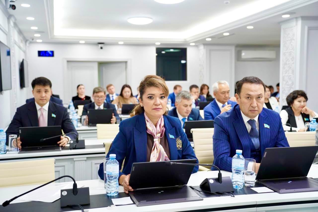 Жиналыс залында ноутбуктерімен отырған ресми киінген адамдар.