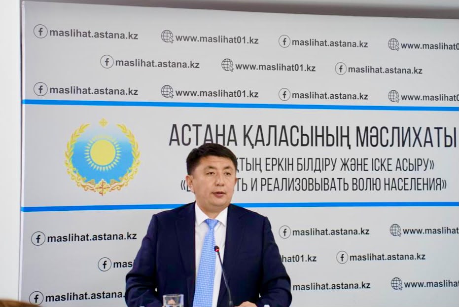 Астана қаласының мәслихатының алдында сөйлеп тұрған костюм киген ер адам.