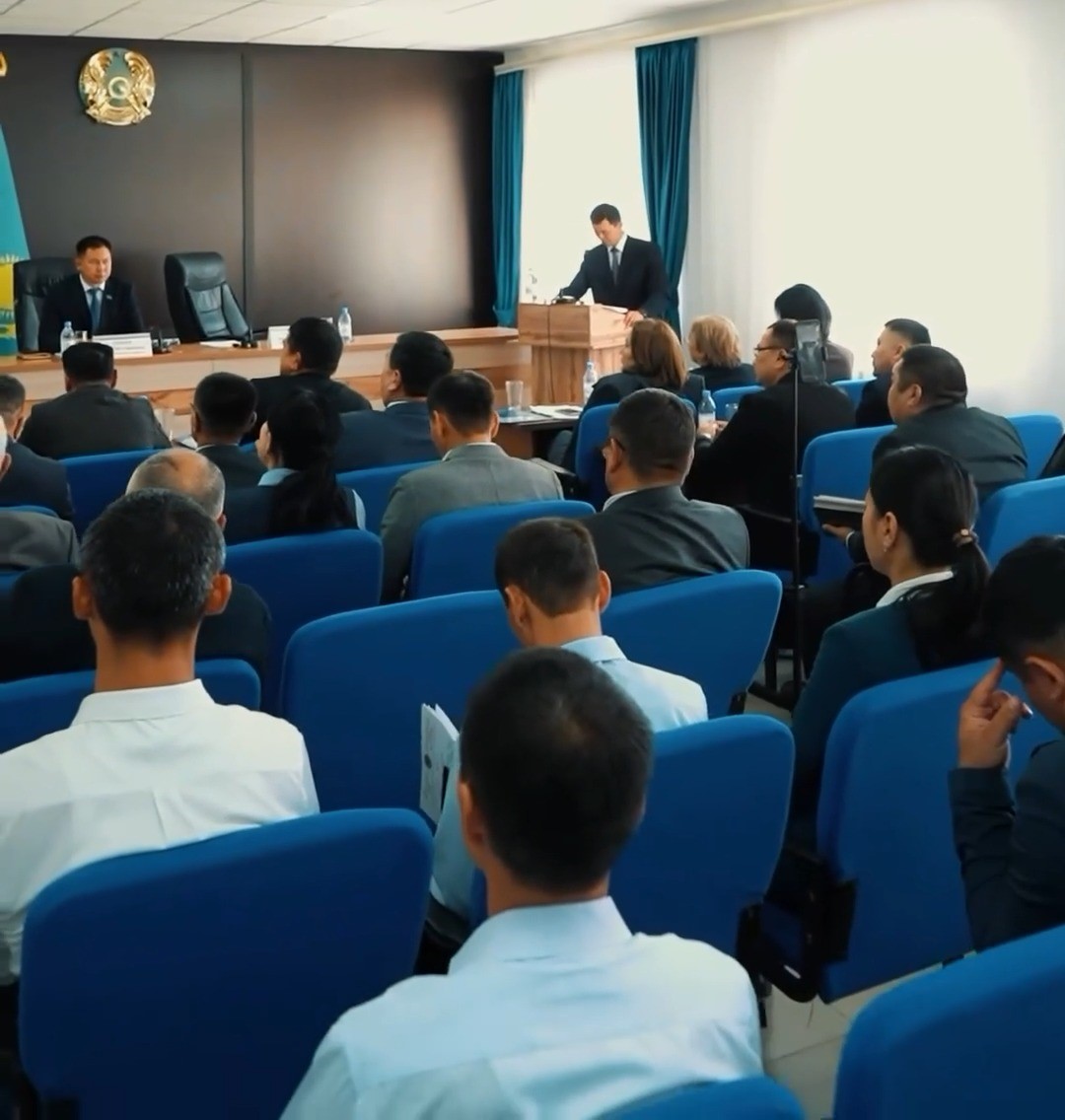 Конференция залындағы жиналыс: трибунада сөйлеп тұрған спикер және тыңдаушылар.