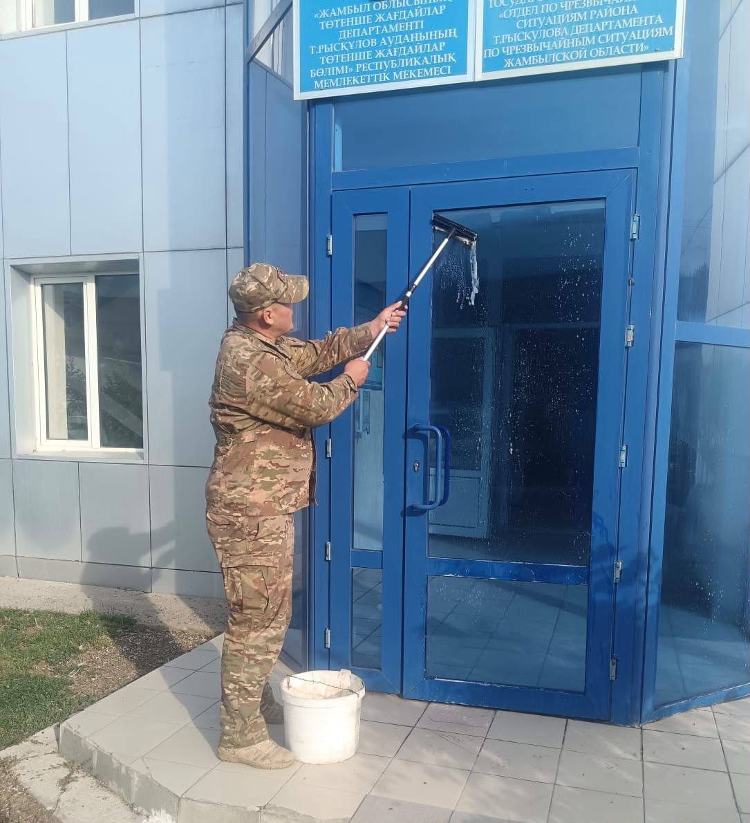 Камуфляж киген адам ғимараттың көк шыны есігін жуып жатыр.