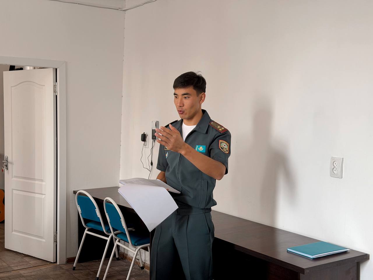 Форма киген ер адам құжаттарды ұстап, бірнәрсе түсіндіріп тұр.