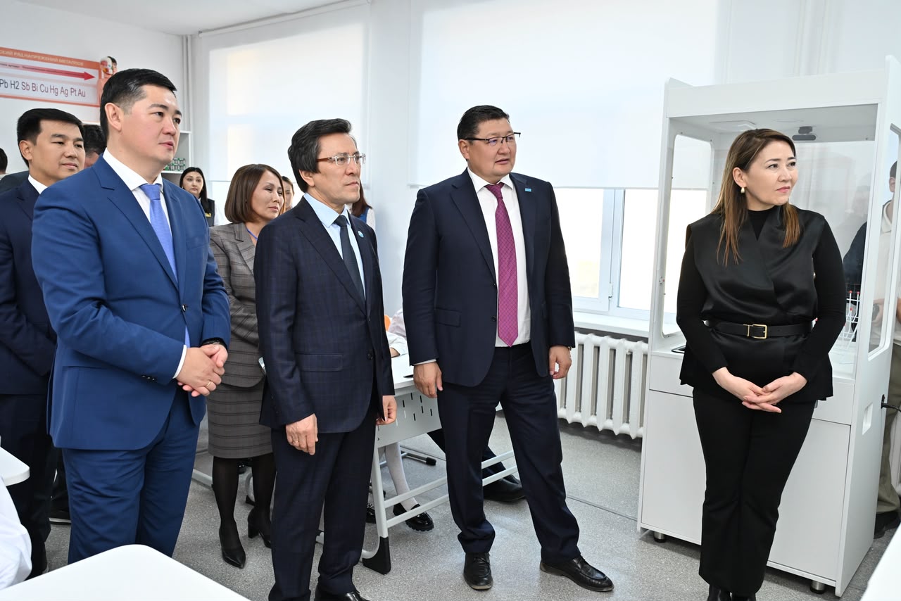 Ресми киімдегі адамдар тобы зертханадағы жабдықты қарап тұр.