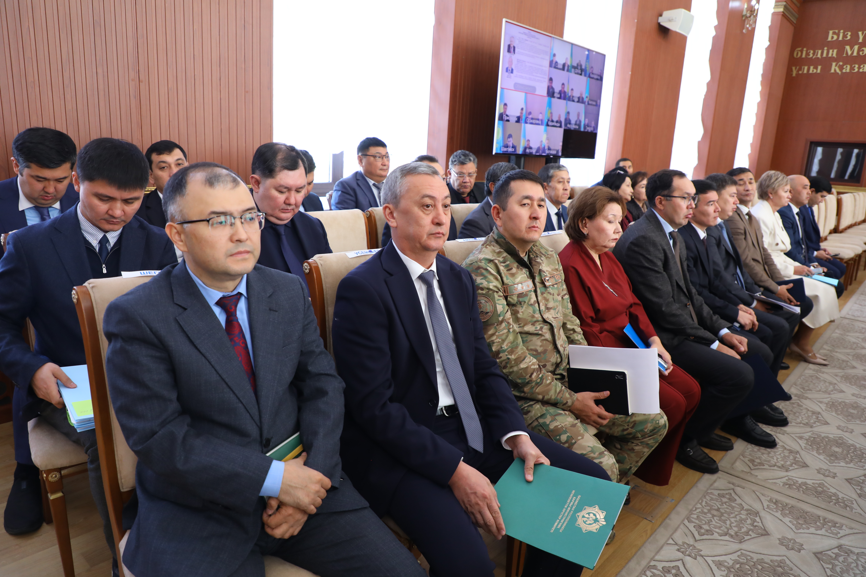Жиналысқа қатысушы костюм киген ресми тұлғалар мен әскери формадағы адамдар.