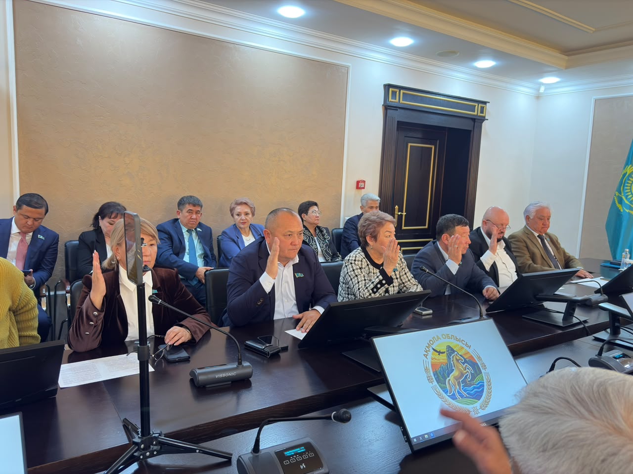 Жиналыс кезінде қол көтеріп дауыс беріп жатқан депутаттар тобы.