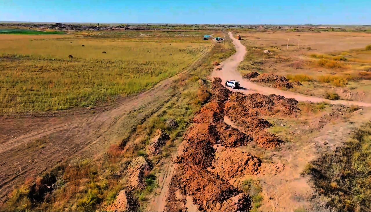 Белый автомобиль на грунтовой дороге в засушливой степи рядом с насыпями из рыжей земли.