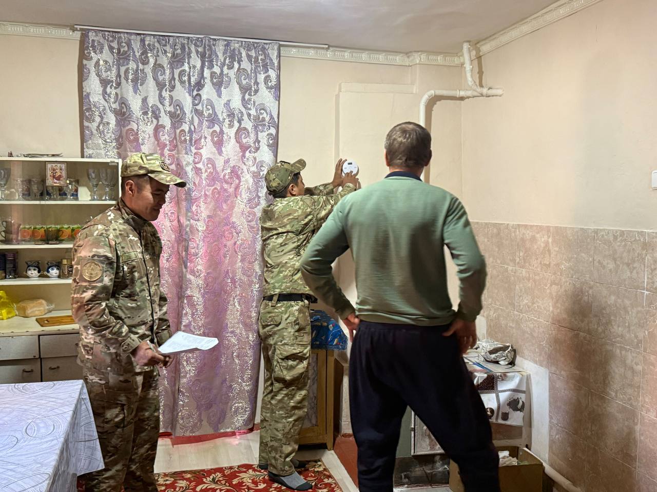 Әскери формадағы адамдар мен ер адамның бөлме ішіндегі тексеру барысы.