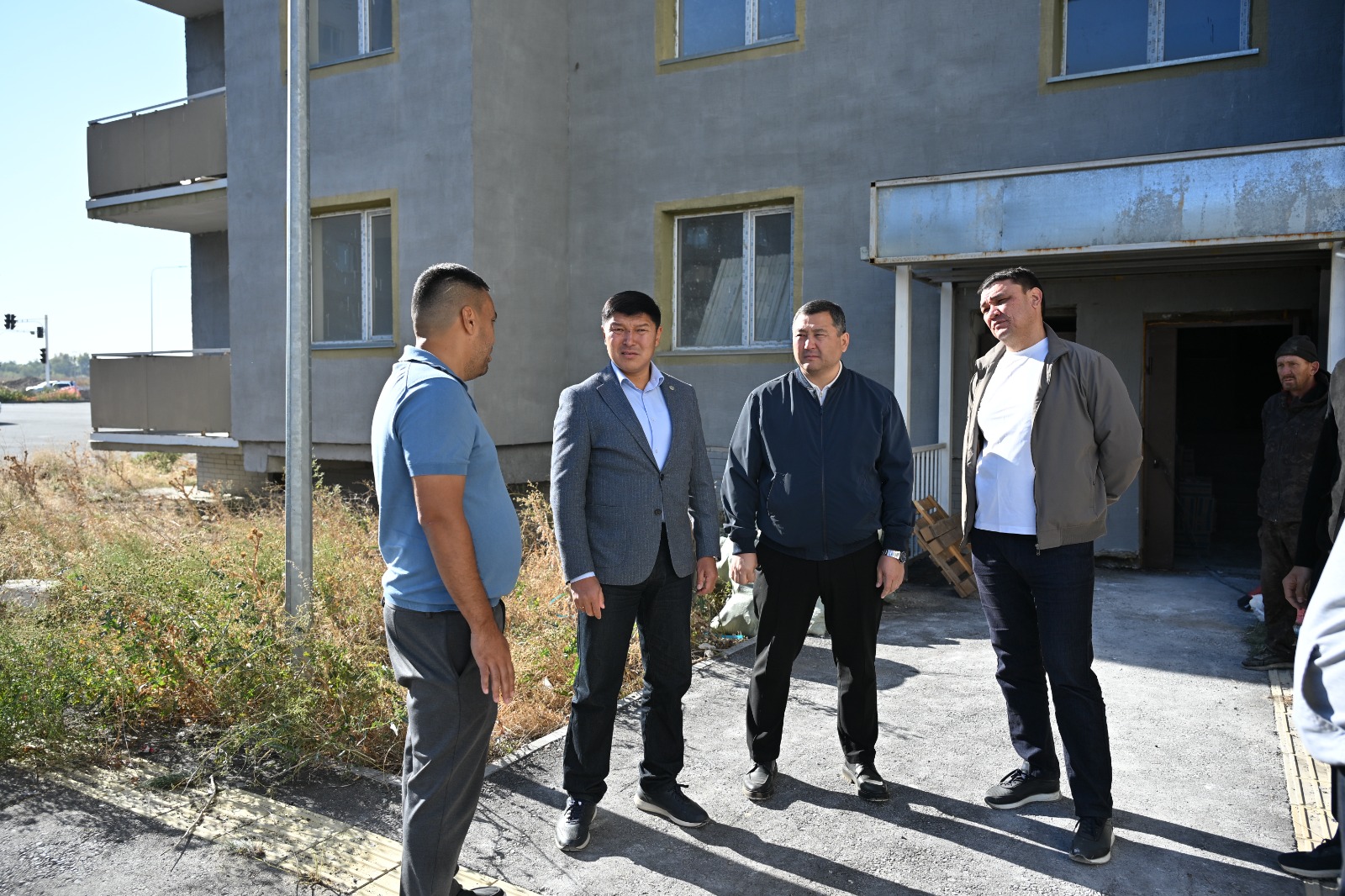 Ғимарат алдында тұрған төрт ер адамның әңгімелесуі.
