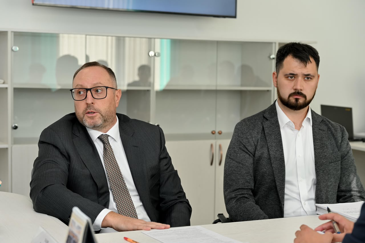 Кісса костюм киген екі ер адам келіссөздер жүргізіп отыр.