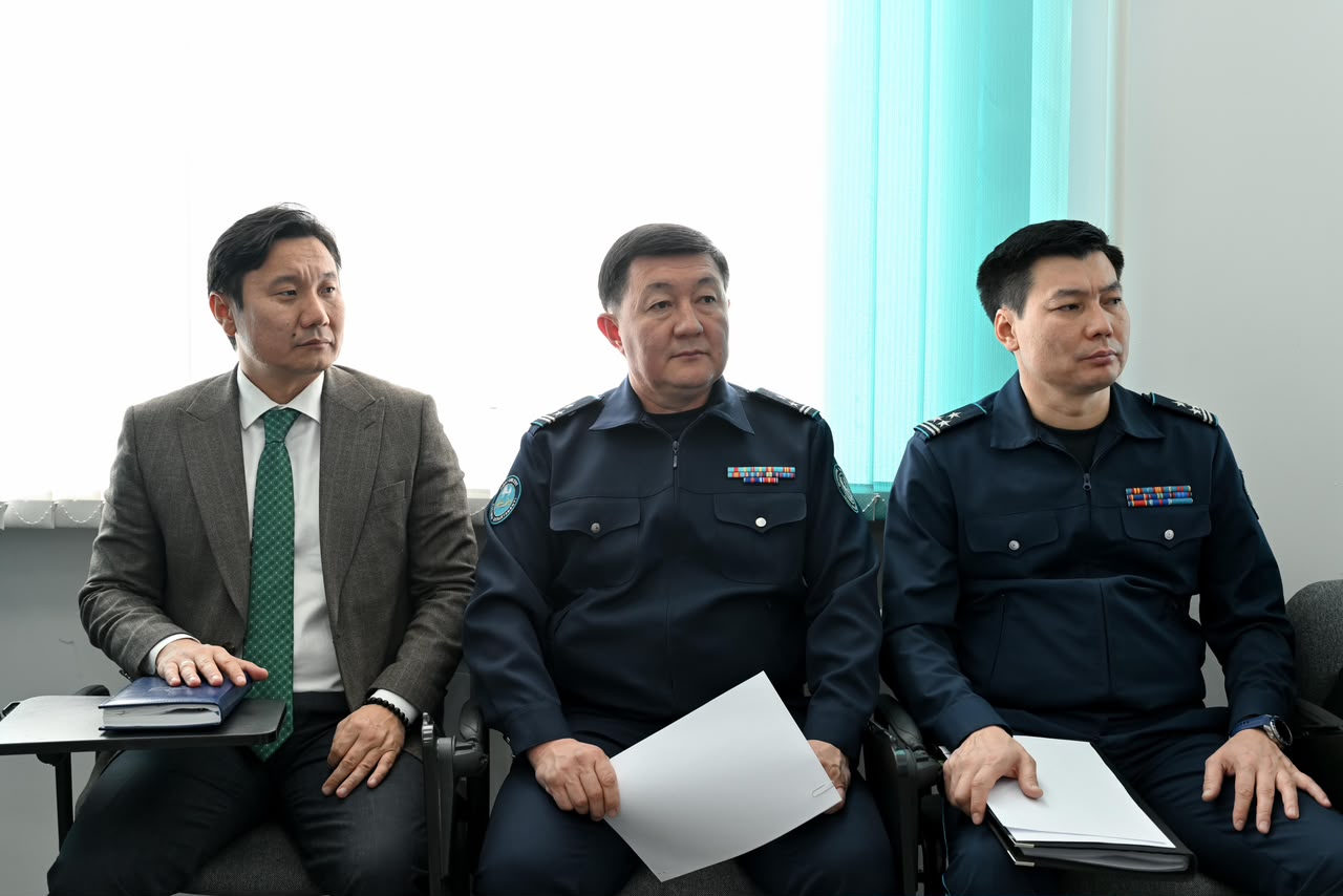 Костюм киген ер адам және екі әскери формадағы маман отырып тұр.