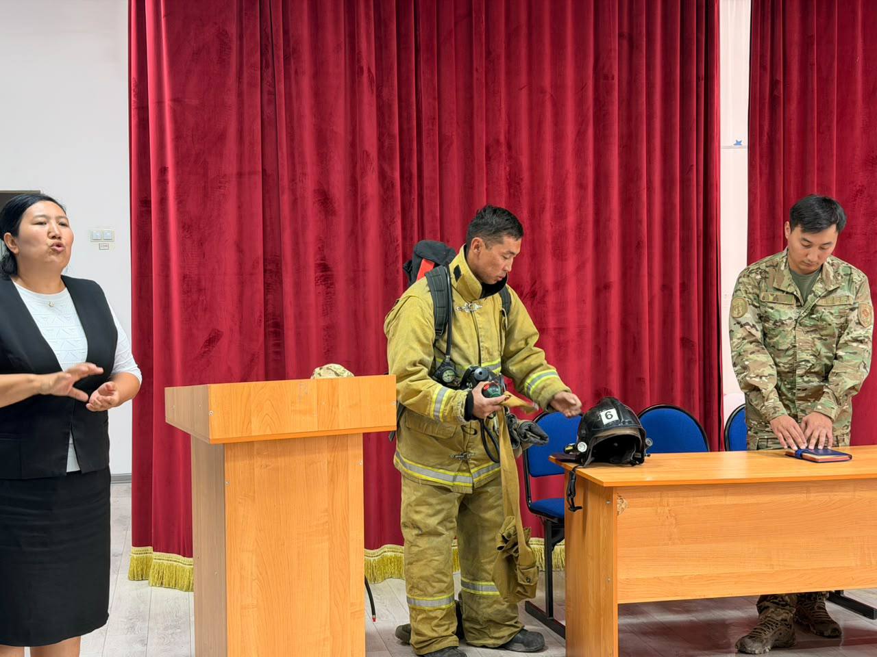 Өрт сөндірушінің арнайы киімі мен жабдықтары туралы презентация жасап жатқан адамдар.