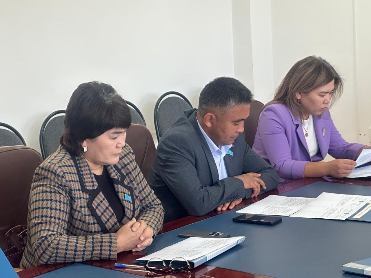 Жыналыс үстелінде құжаттарды қарап отырған үш әріптес.