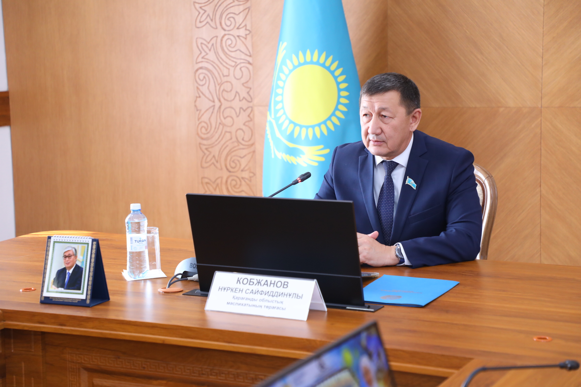 Қазақстан Республикасының Туының алдында үстел басында отырған Нүркен Кобжанов.