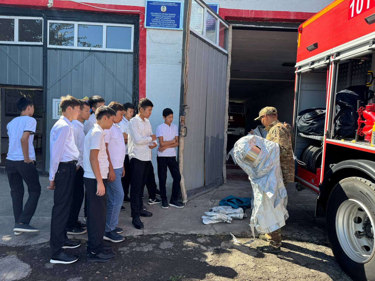 Өрт сөндірушінің арнайы киімін таныстырылуын бақылап тұрған оқушылар тобы.