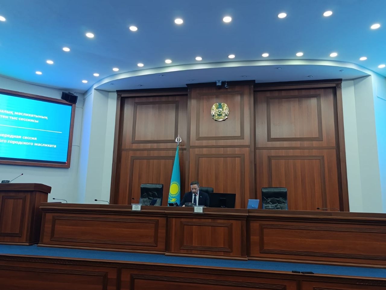 Қазақстан Республикасының мемлекеттік гербі мен туы бар мәжіліс залындағы отырыс.