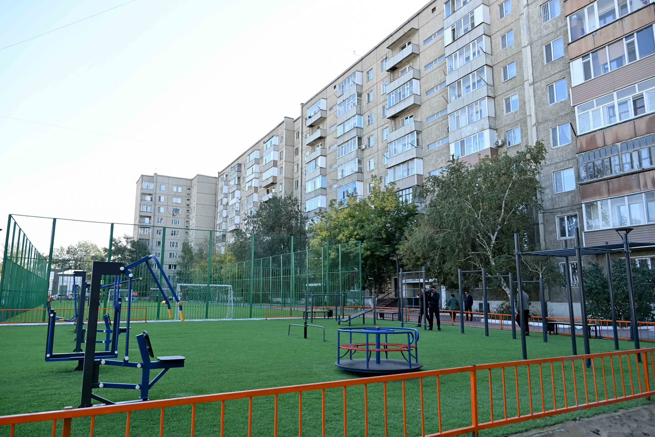 Көпқабатты үйлердің алдындағы жасанды шөпті алаңы бар заманауи спорт алаңы.