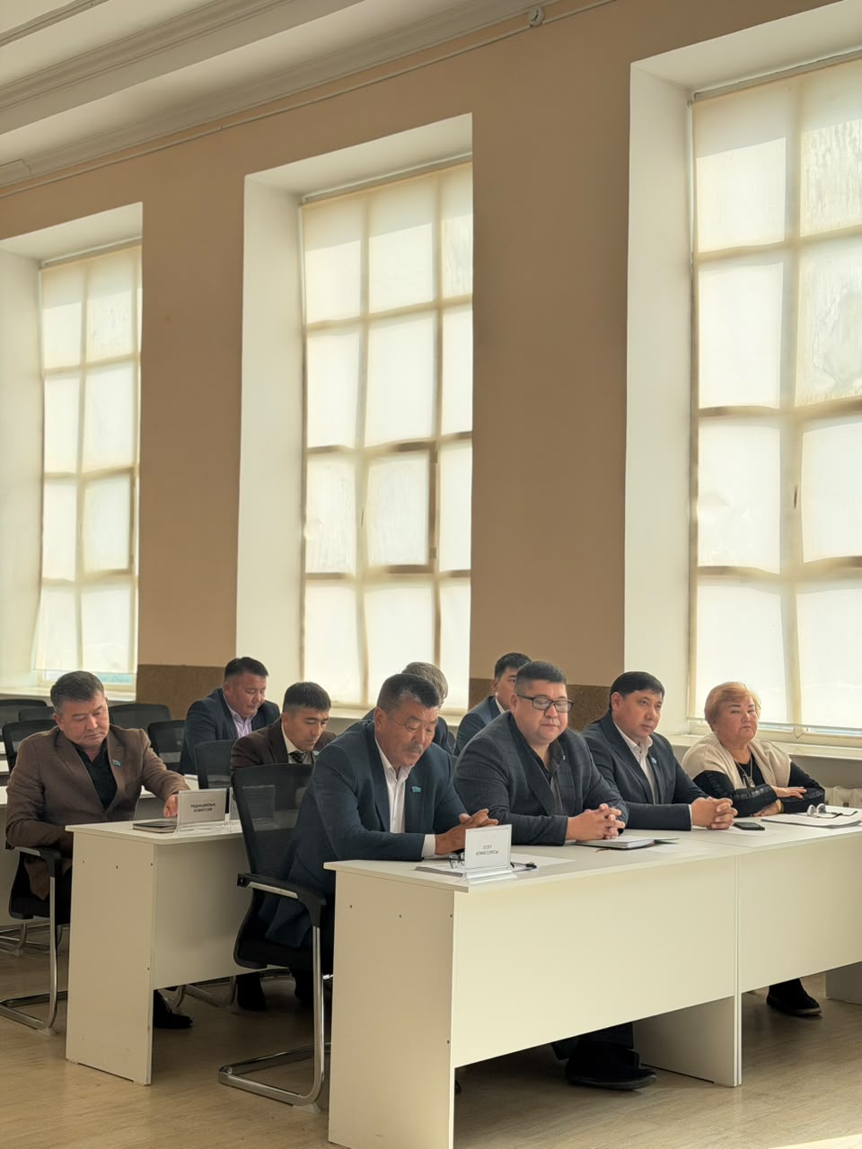 Жиналыс үстелінде отырған ресми киінген адамдар тобы.
