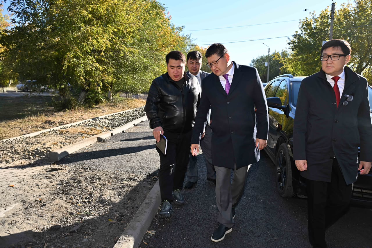 Группа мужчин в деловой и повседневной одежде идет по краю новой асфальтированной дороги на фоне осенних деревьев.