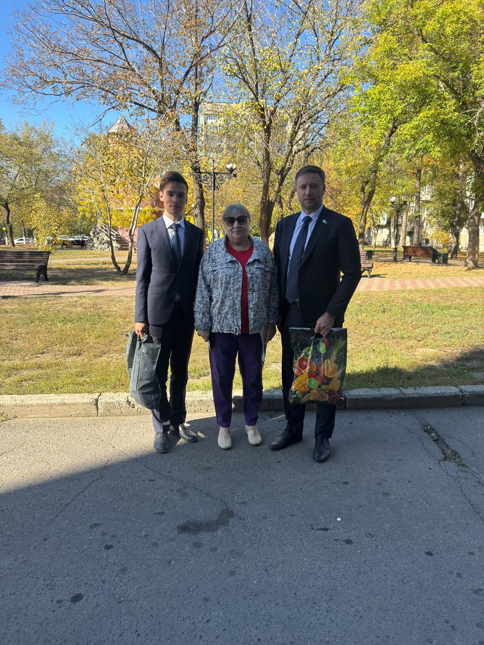 Күзгі саябақта тұрған екі костюм киген ер адам мен бір әйел.