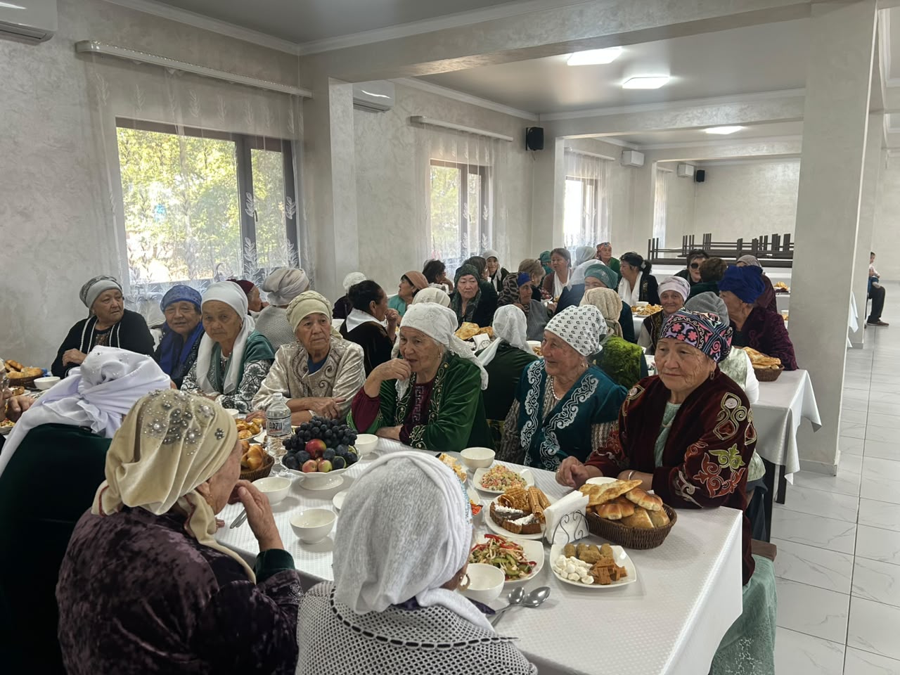 Ұлттық киім киген қария әйелдердің дастархан басында жиналып, әңгімелесіп отырғаны.