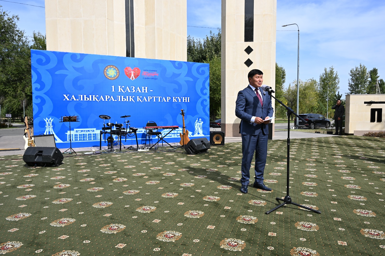 Халықаралық қарттар күніне арналған іс-шарада сөйлеп тұрған ер адам.