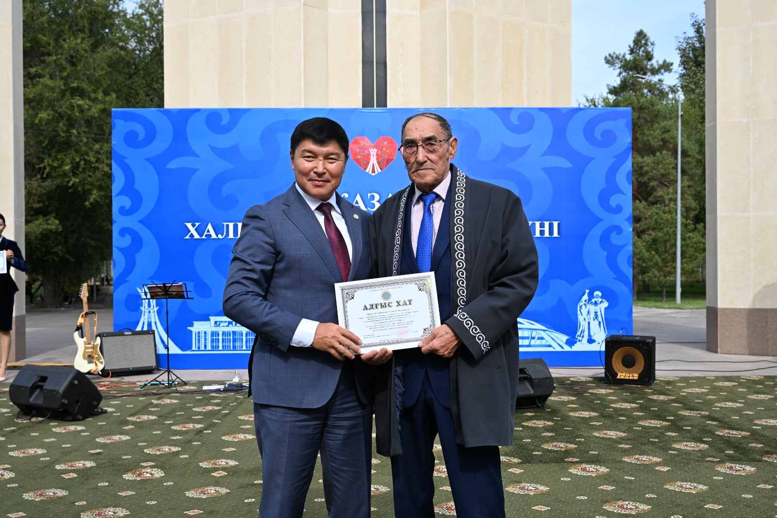 Екі ер адамның алғыс хатты ұстап тұрған суреті.