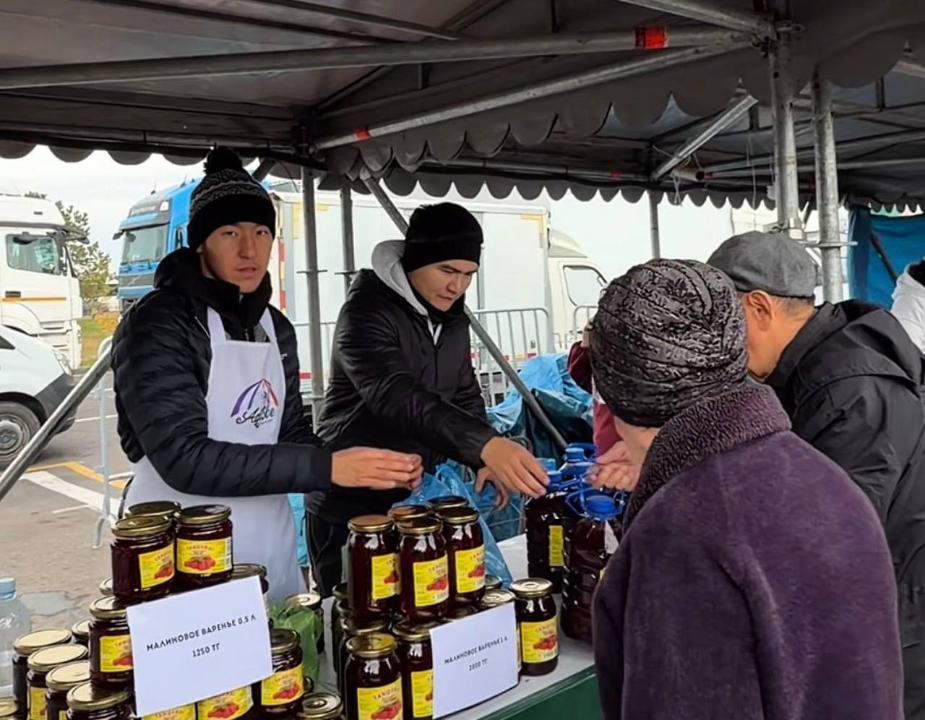 Көшедегі сауда нүктесінде екі сатушы сатып алушыға банкадағы вареньелерді ұсынып жатыр.