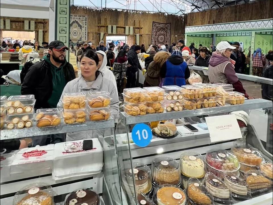 Пісірмелер мен тәттілер сатылатын жәрмеңкедегі сатып алушылар мен сатушылар.