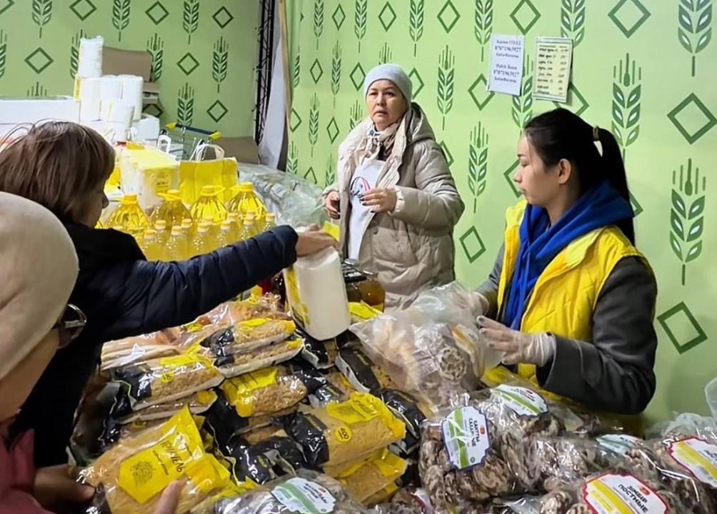 Азық-түлік дүкеніндегі сатушы мен сатып алушылар. Сөреде май, нан және басқа да тағамдар жатыр.