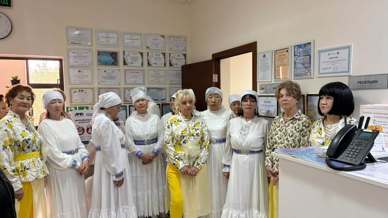 Ұлттық киім киген әйелдер тобы кеңседе тұр.