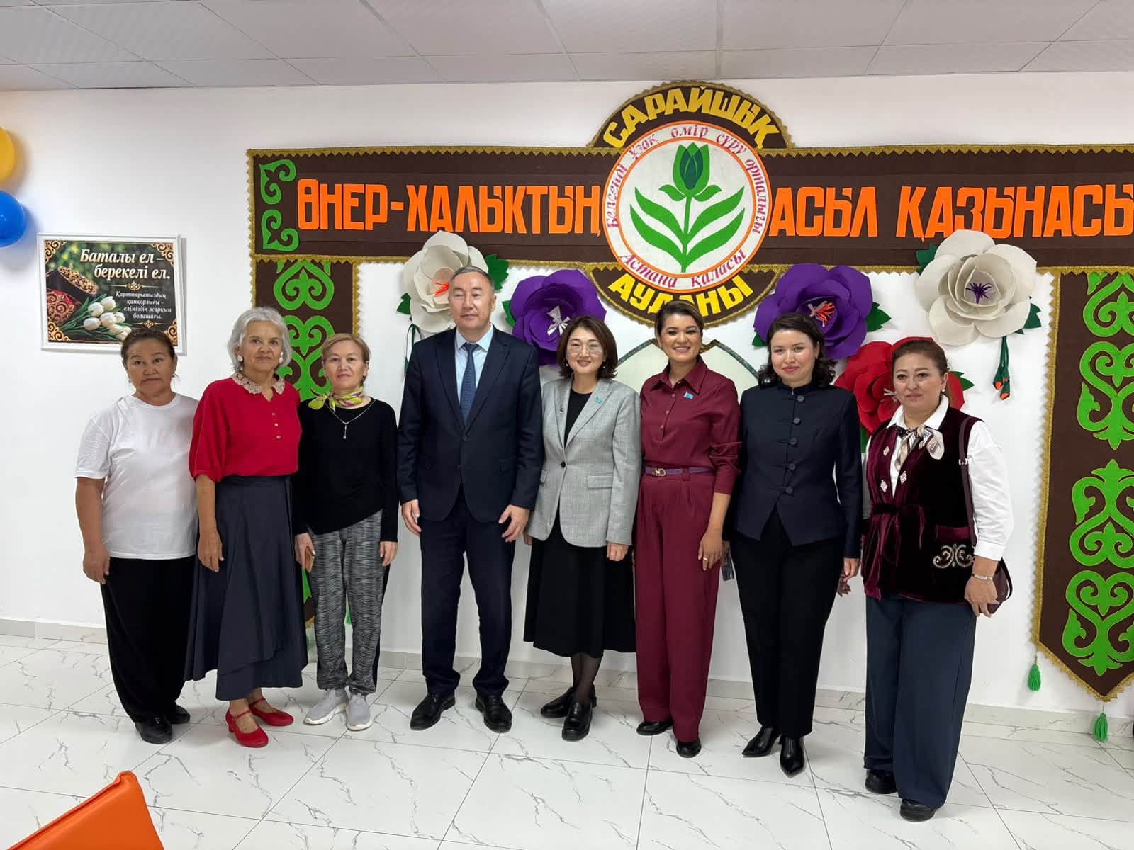 «Өнер-халықтың асыл қазынасы» жазуы бар фонның алдында тұрған адамдар тобы.