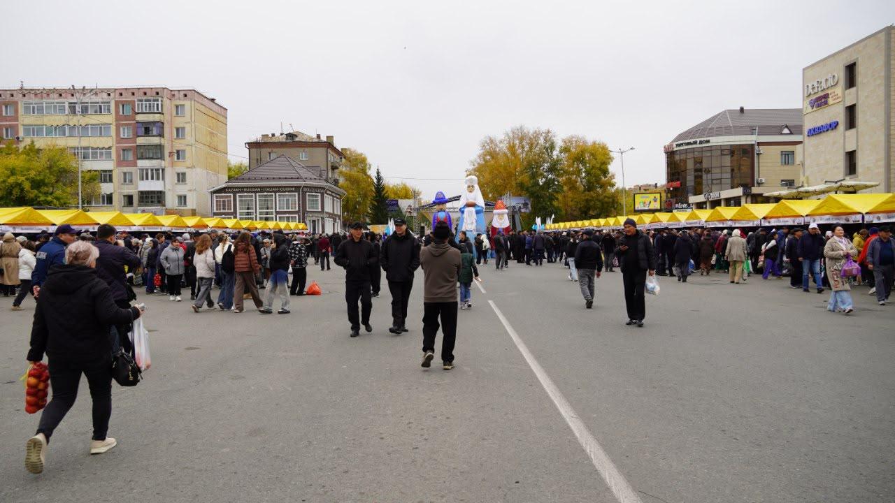 Люди на открытом рынке с желтыми тентами на фоне городских зданий в пасмурный день.
