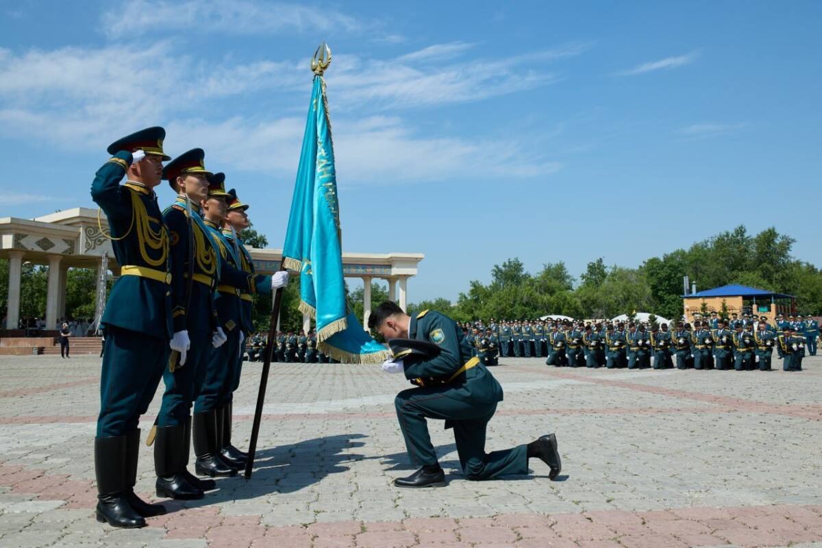 Әскери формадағы саптығы салдаттар және ту алдында тізе бүгіп, серт беріп жатқан әскер.