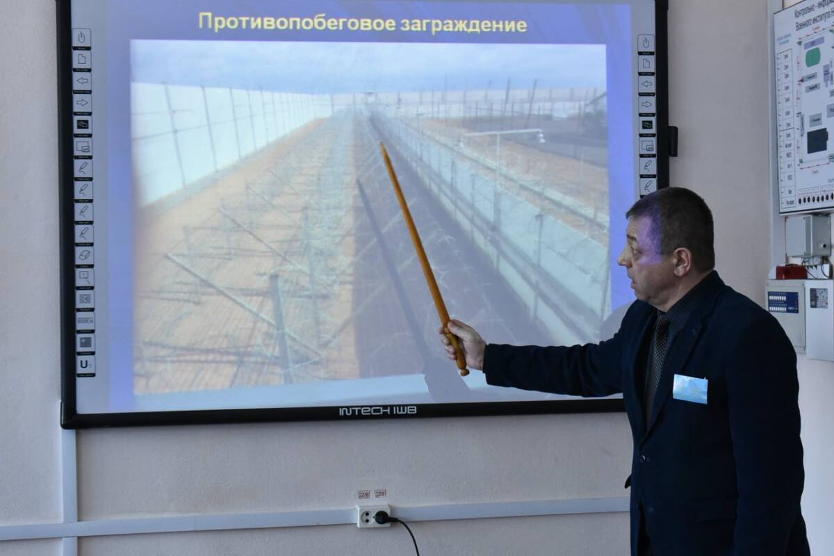Интерактивті тақта алдында тұрған ер адам көрсеткішпен қоршаудың суретін түсіндіріп жатыр.