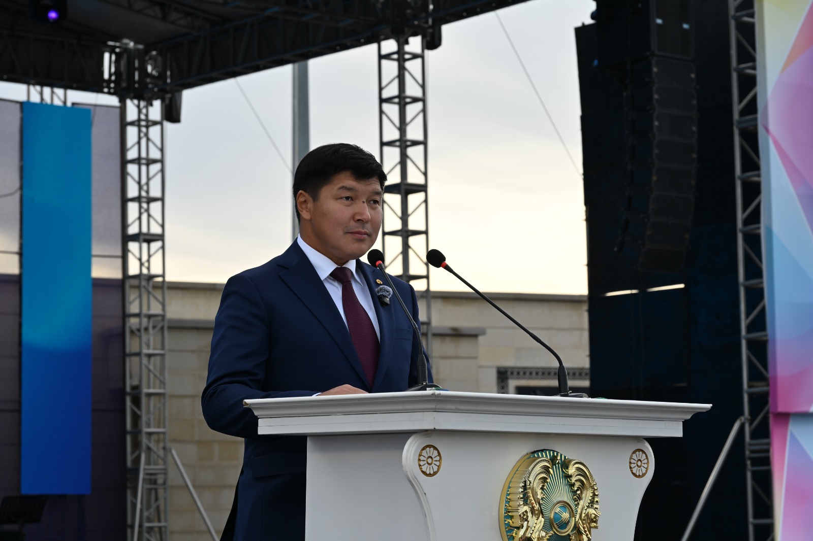 Кіссада тұрып сөйлеп жатқан костюм киген ер адам.